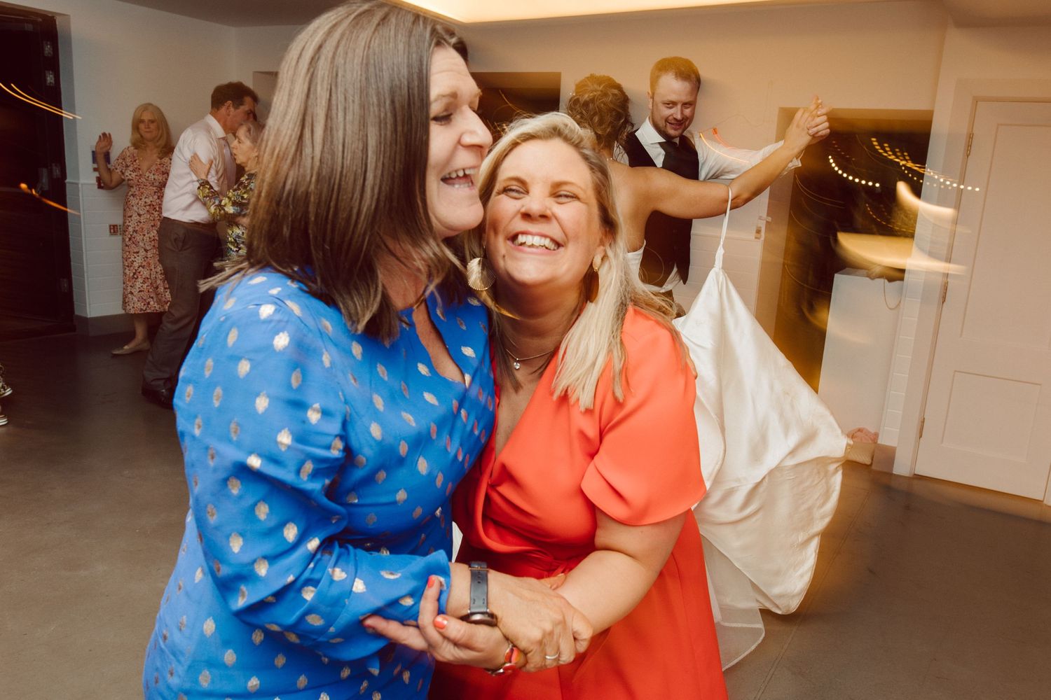Wedding guests dancing and embracing during a festive celebration indoors.