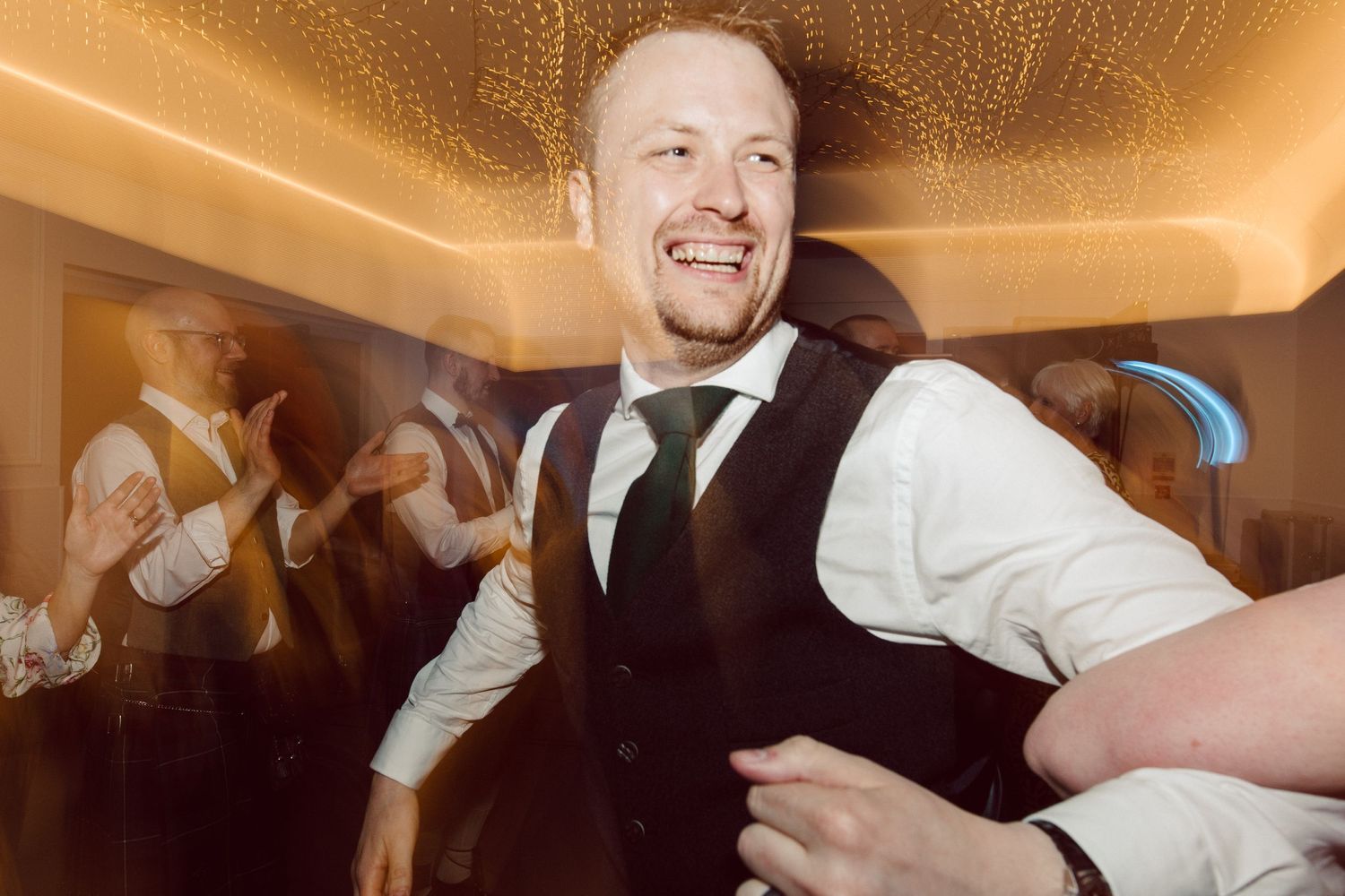 Wedding guests enjoying energetic dancing under warm lighting at a reception venue.
