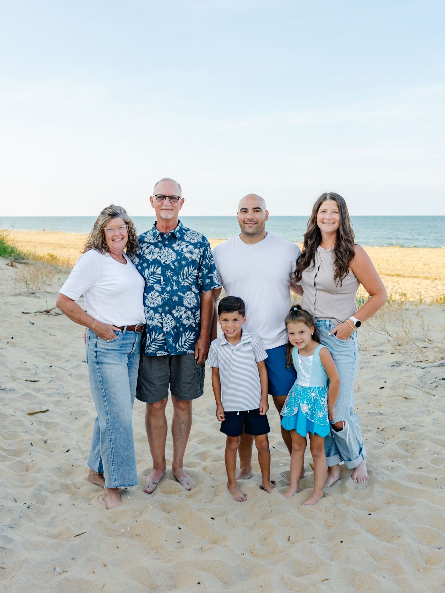 Family group poses together on sandy beach at sunset wearing casual summer outfits.