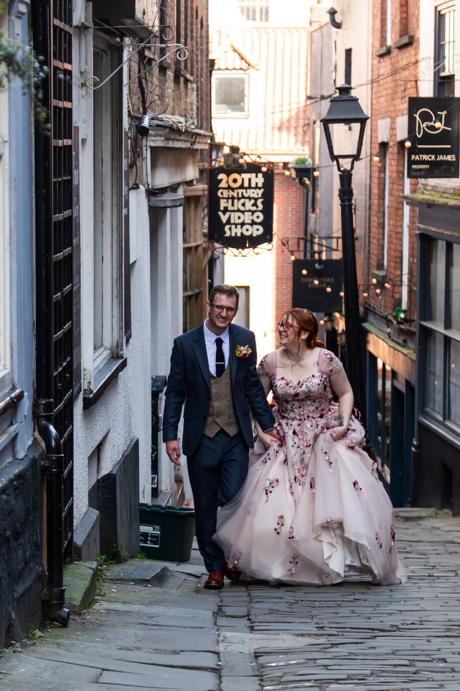 Wedding couple walking down a charming cobblestone street between historic brick buildings.
