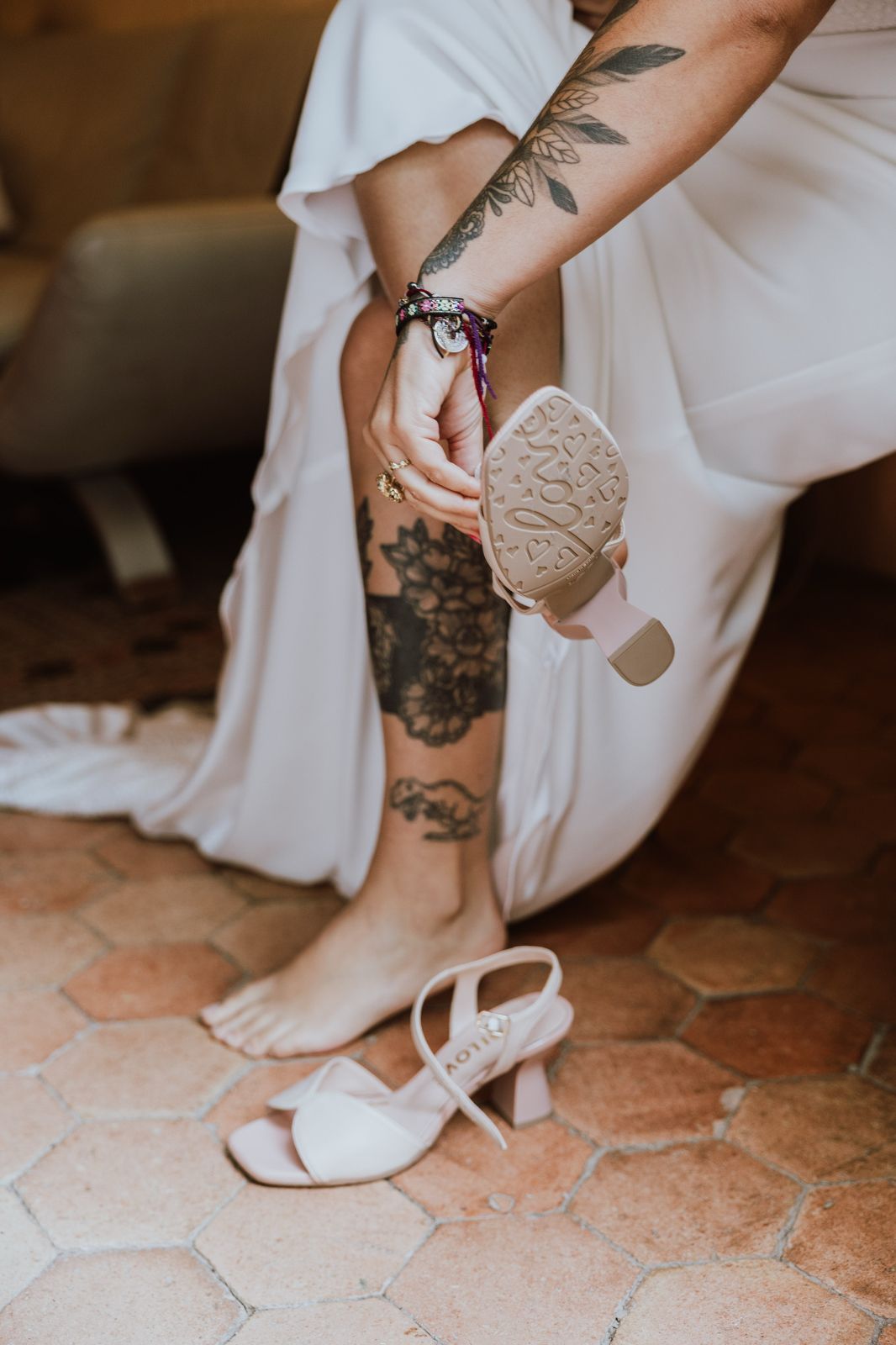 White wedding shoes and visible leg tattoos on terracotta tile flooring in an elegant bridal setting.