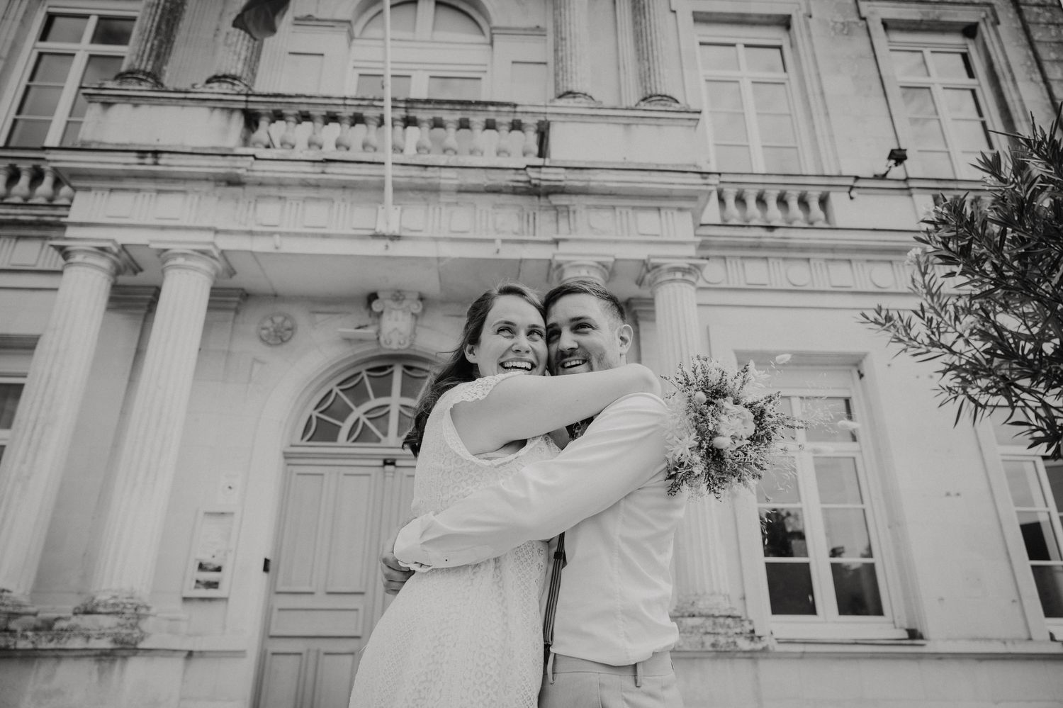 Bride and groom share a joyful moment together in front of an elegant white building facade.