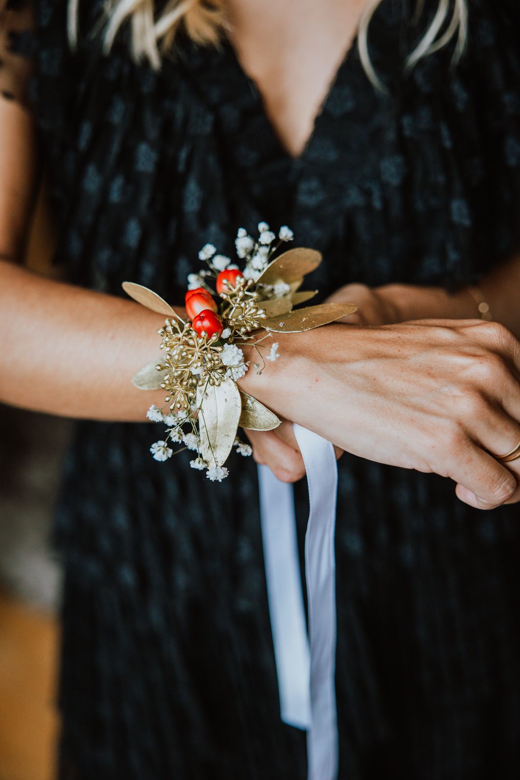 Close-up view of delicate baby's breath and red ladybug corsage being placed on someone's wrist.