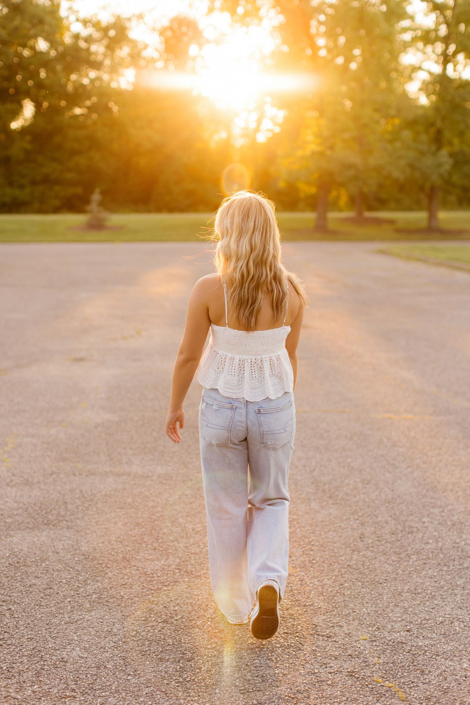Person walking away on path during golden sunset wearing white top and light jeans.