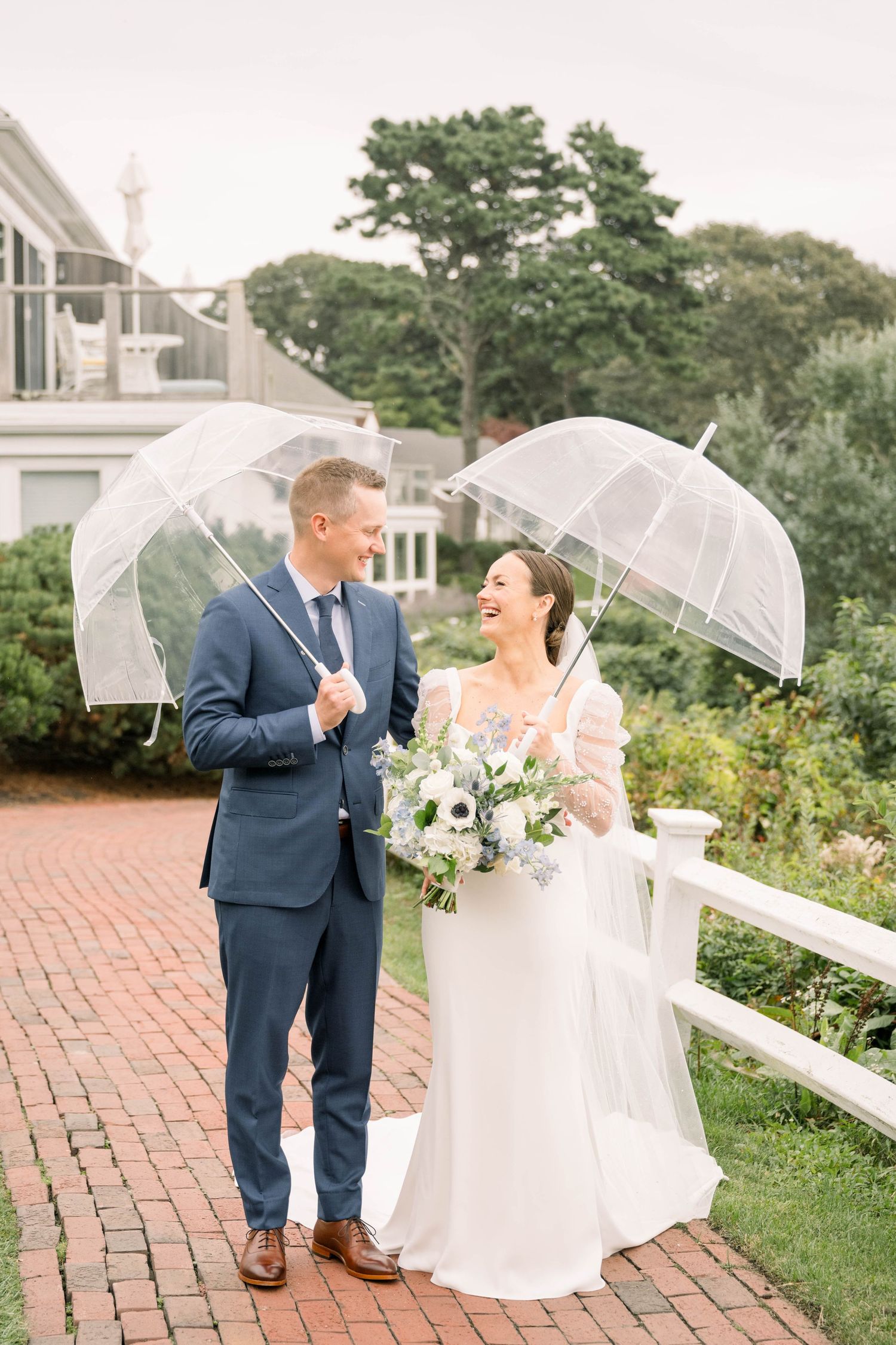 A seaside wedding portrait with a couple in white attire against a coastal mansion backdrop.