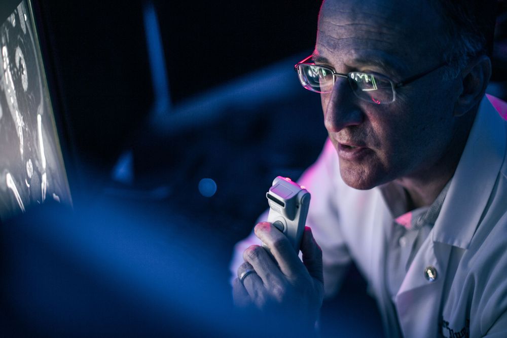Medical professional in white coat examining diagnostic screen with blue lighting in dark laboratory setting.