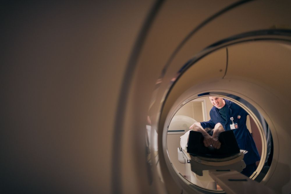 View through a circular opening showing a radiology technician working with medical scanning equipment.