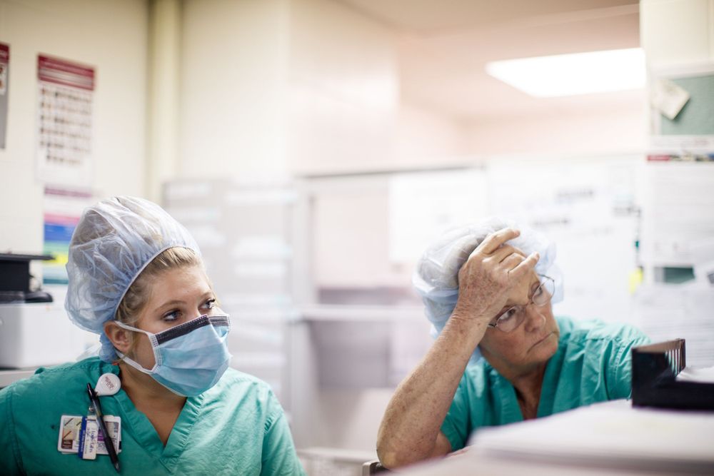 Healthcare workers in scrubs and PPE look tired and stressed during their shift in a medical facility.