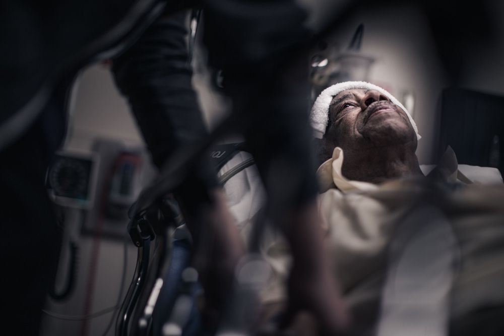 Medical patient lies under surgical lighting in a dramatic composition with dark shadows and bright illumination.