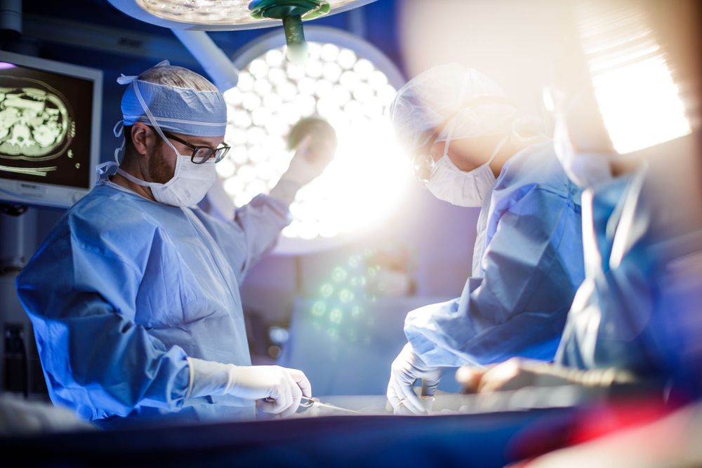 Medical team performs surgery under bright surgical lights in an operating room with blue-tinted lighting.