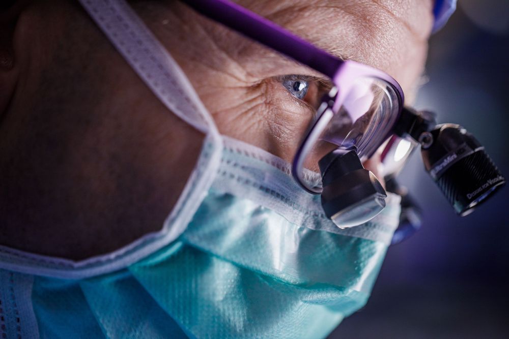 Close-up view of a surgeon wearing surgical loupes and a face mask during a medical procedure.