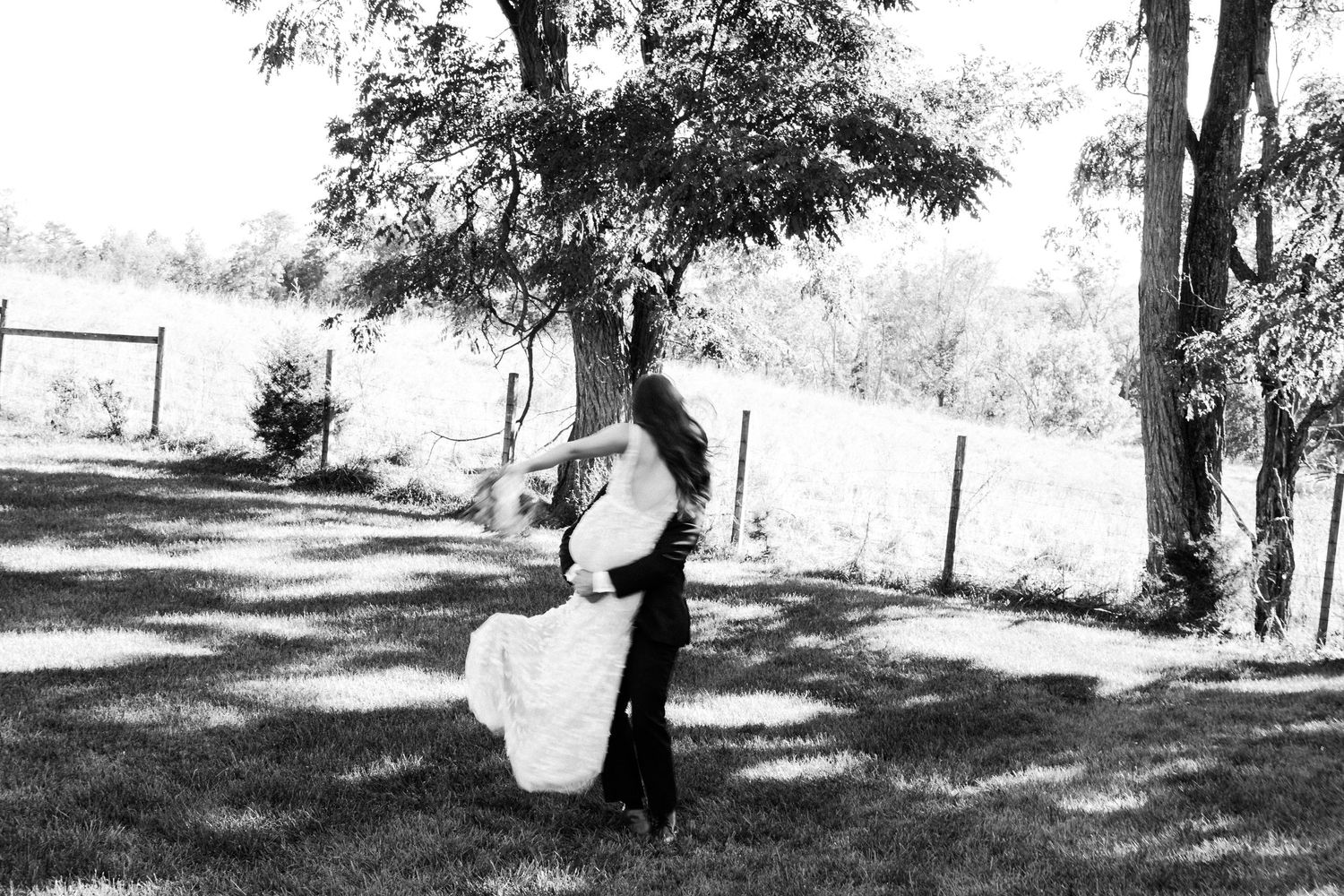A black and white photo shows a person in vintage attire hanging laundry on a clothesline in a shaded backyard.