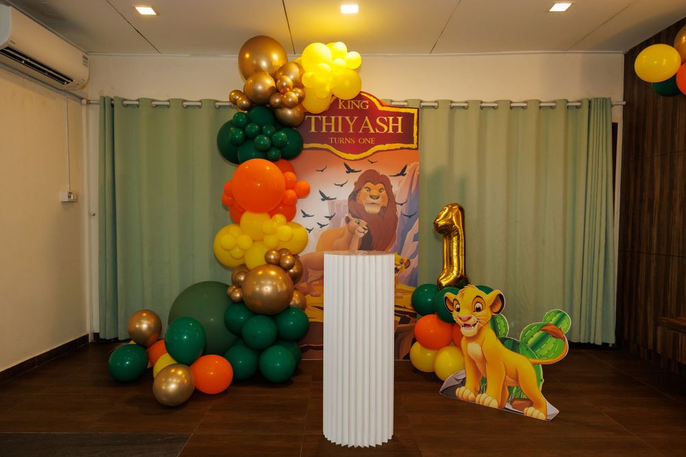 Lion King themed first birthday party decoration with green and orange balloon arch and display column.