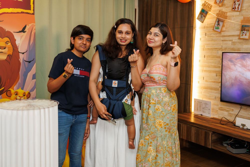 Three people pose together at a party with decorated wall and TV screen in background.