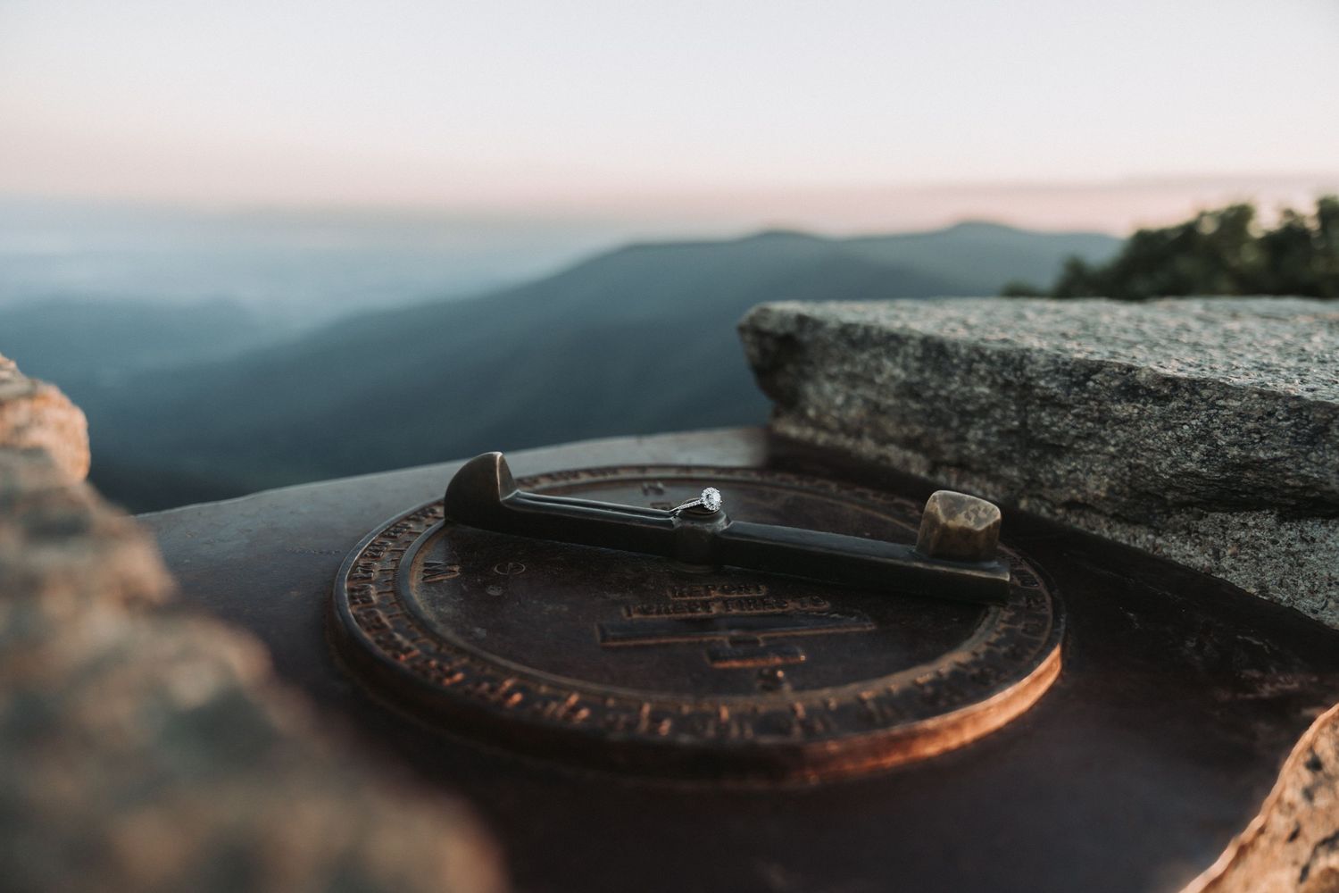 Wedding rings placed on a vintage wooden compass against a mountain landscape backdrop at sunset.