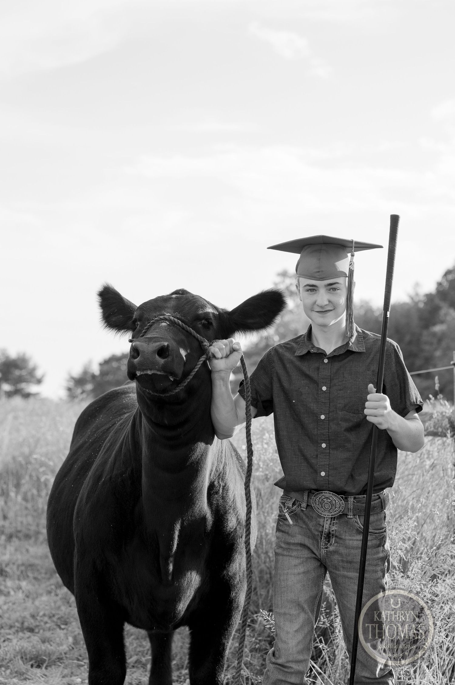 A black and white photo shows a graduate with their show cow in a rural field setting.