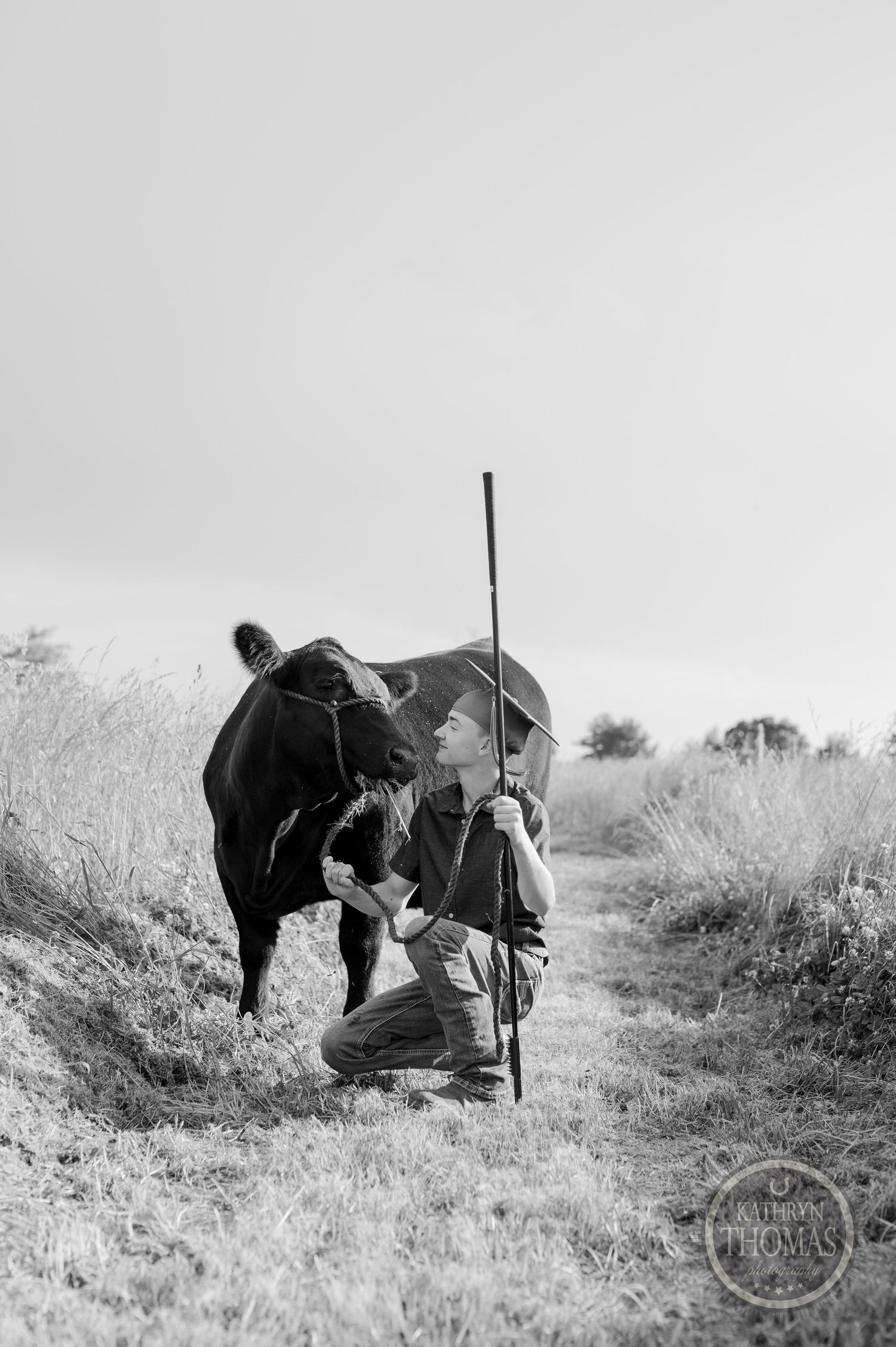 Black and white portrait of person tending to cow on grassy path.