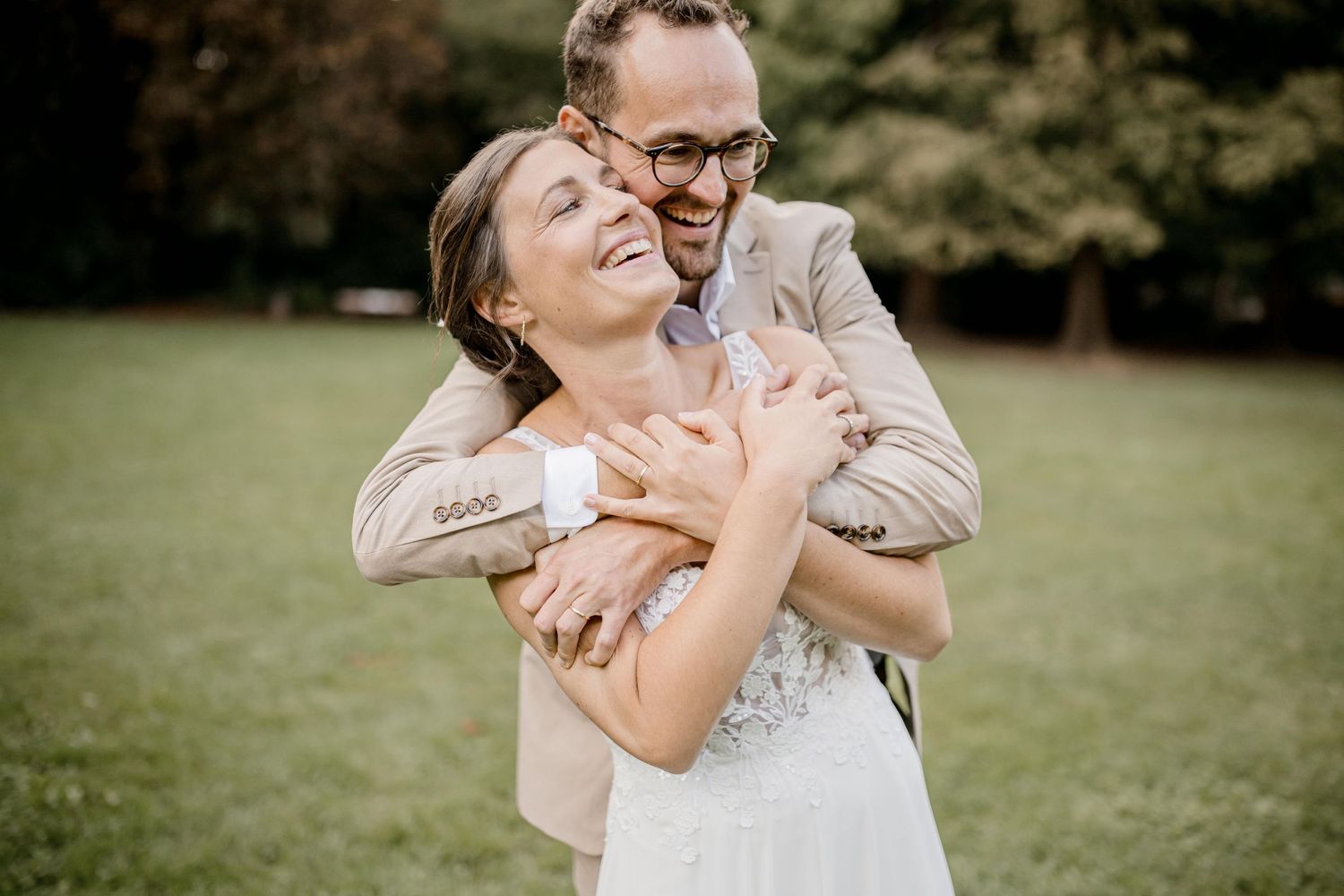 Un couple de mariés joyeux s'embrasse et rit ensemble sur une pelouse herbeuse lors d'une séance photo en extérieur.