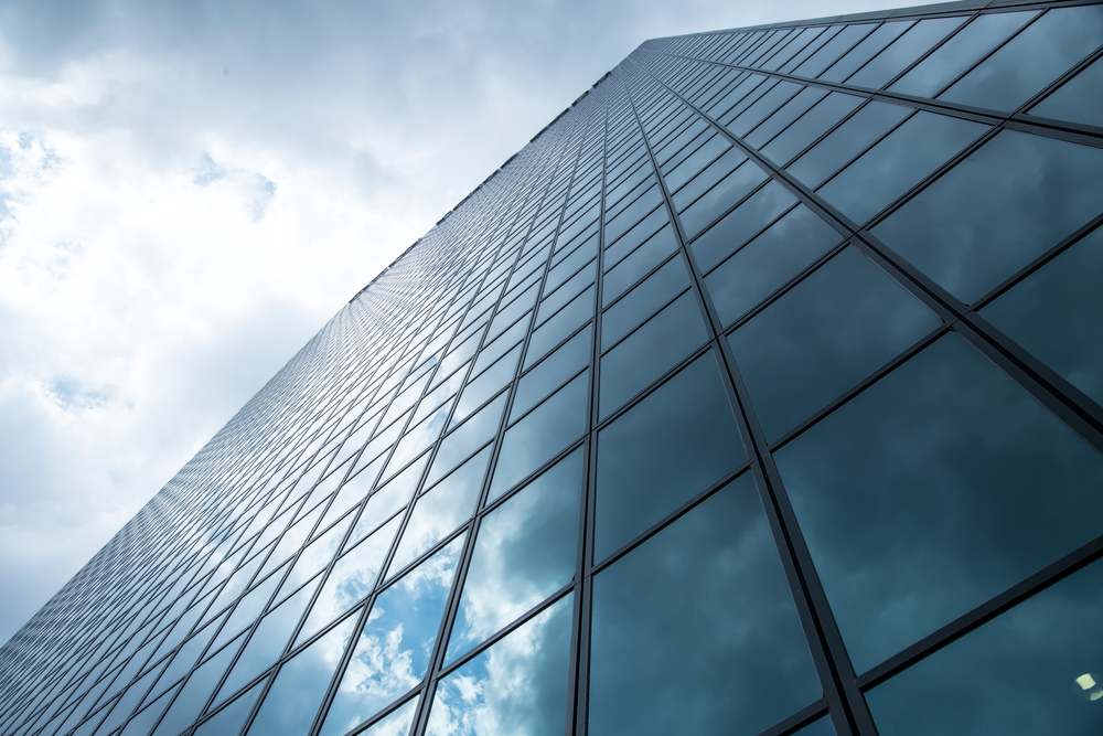 Glass and steel office building facade reflecting blue sky and white clouds.