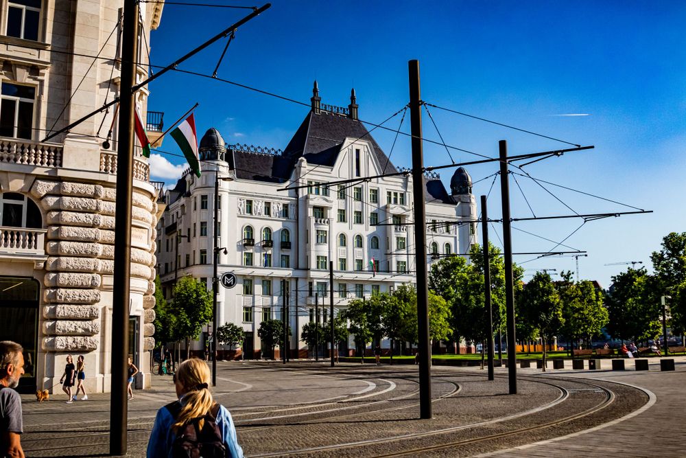Modern white apartment building with gothic architectural elements along a tram line.