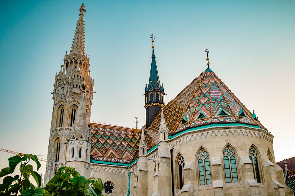 Matthias Church's colorful tiled roof and Gothic spire against turquoise sky in Budapest.