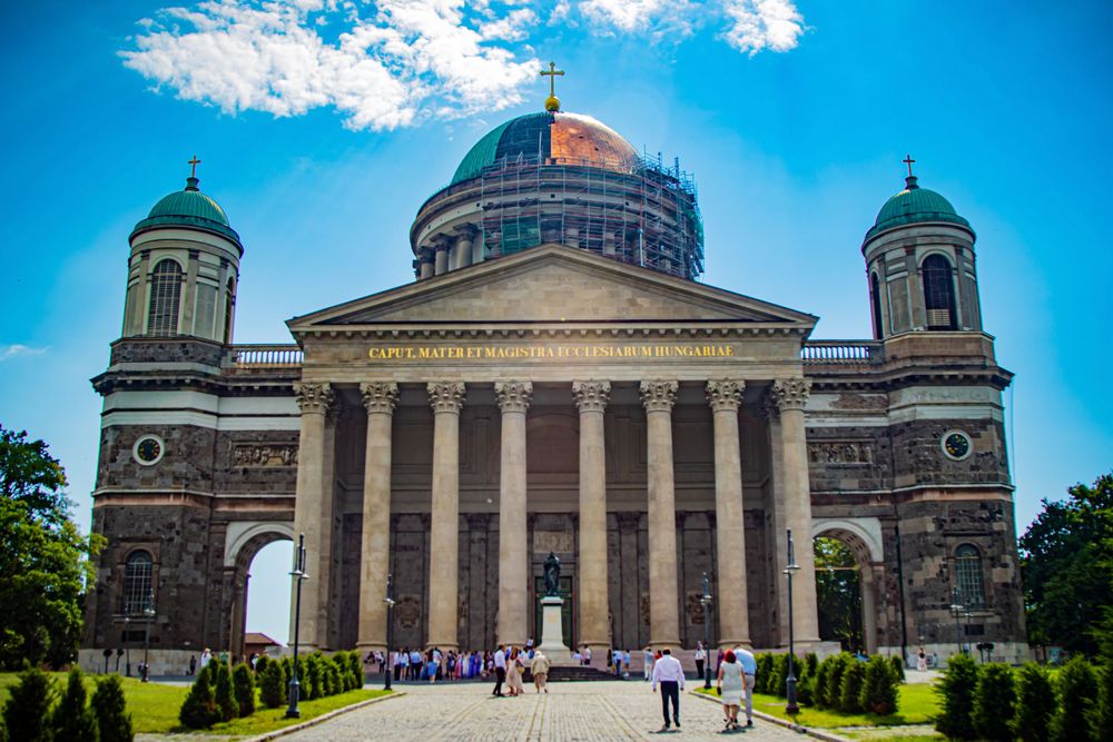 Grand cathedral with symmetrical towers and central dome viewed from the front entrance path.