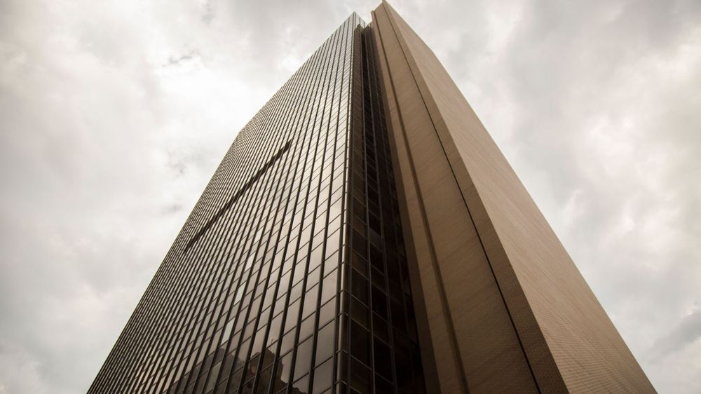 Dramatic upward view of a modern skyscraper with geometric patterns against cloudy sky.