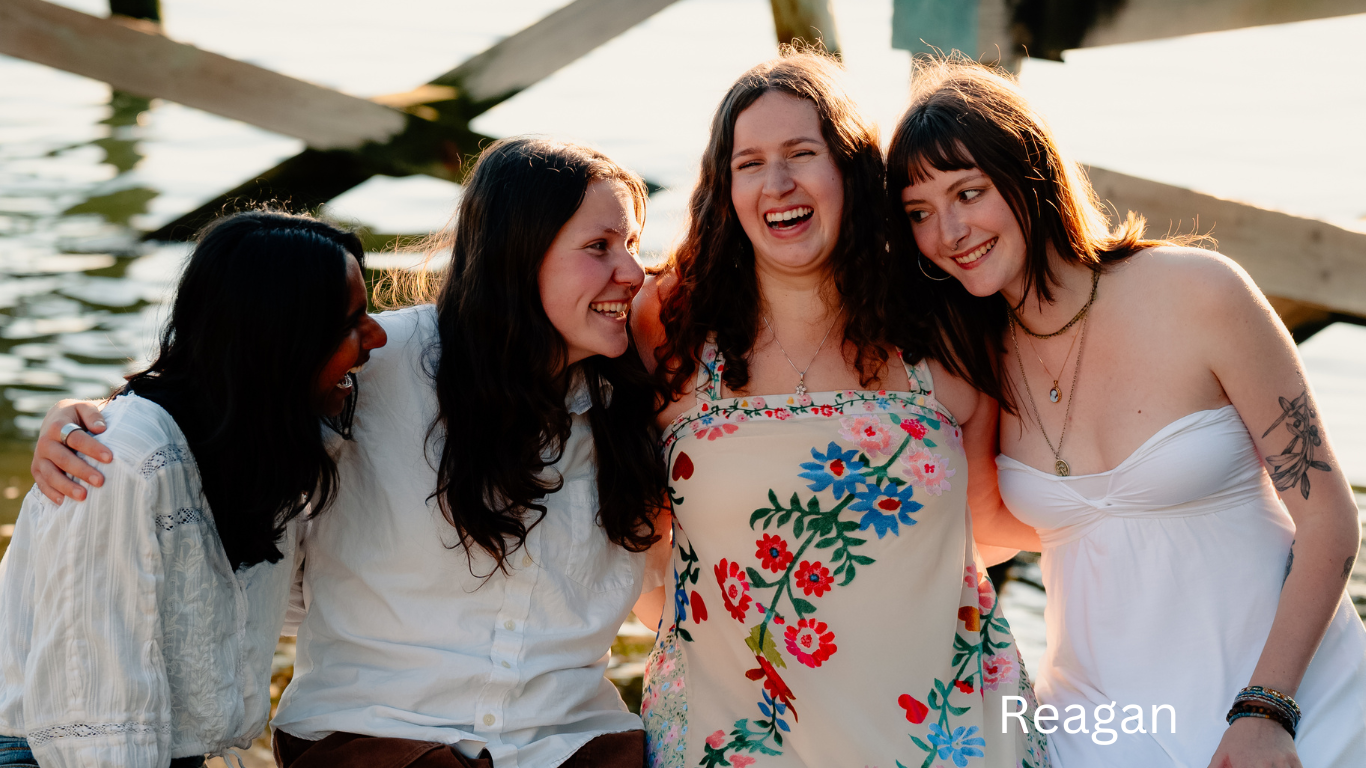 Four friends laughing together at an outdoor gathering wearing casual summer attire.