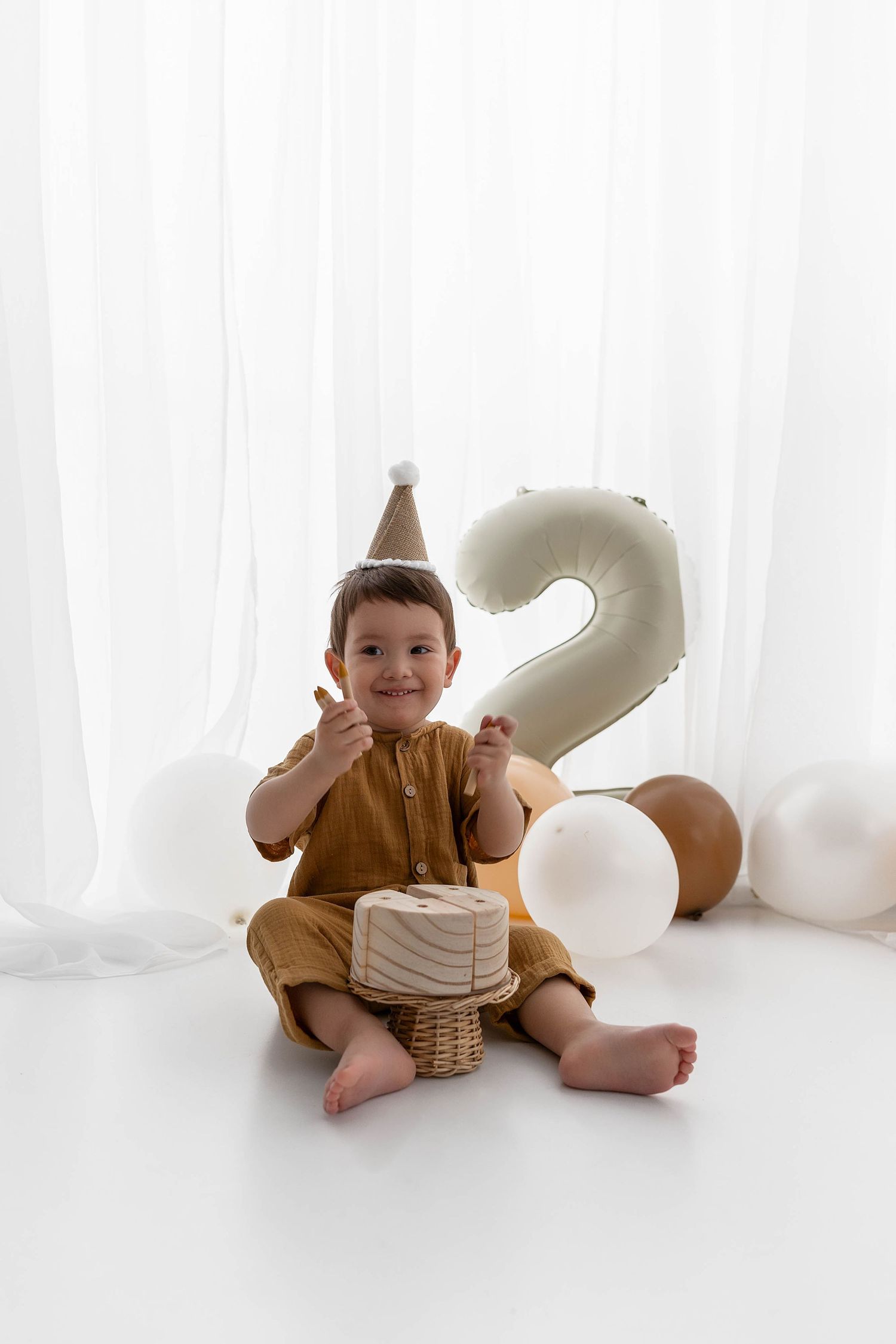 Smiling child wearing party hat with birthday cake and number 2 balloon decoration.
