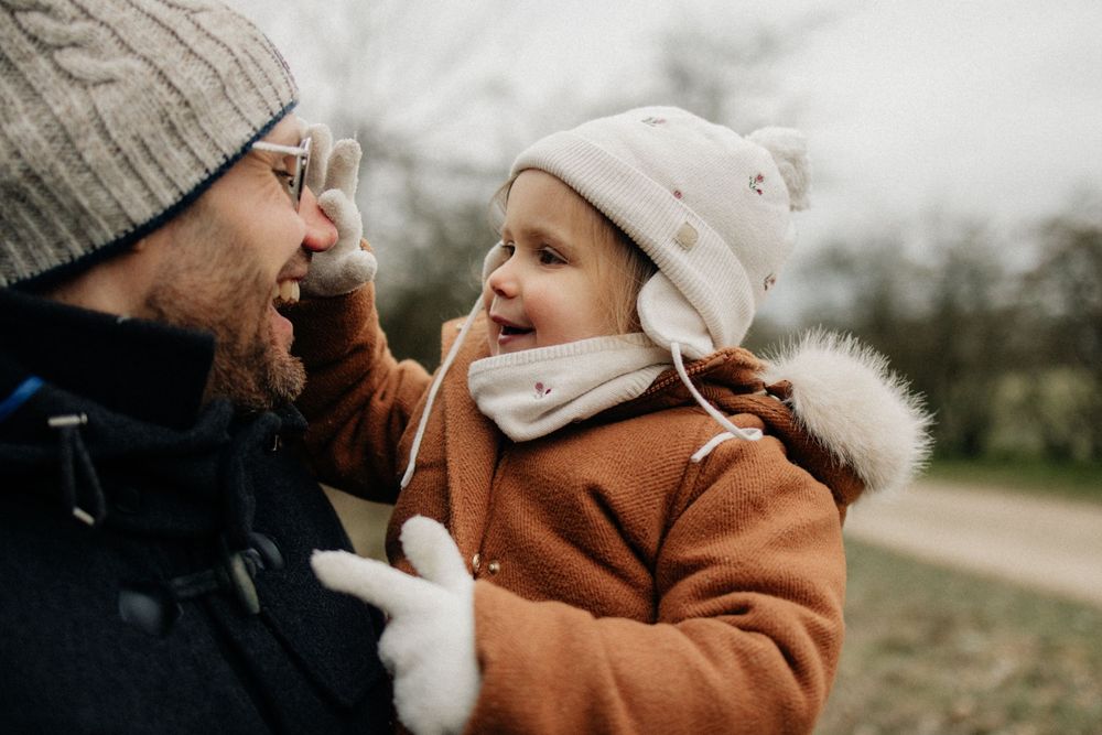 A joyful moment captured between adult and child wearing winter coats and hats during an outdoor walk.