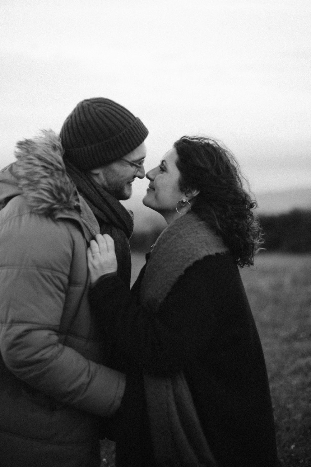 A couple shares an intimate kiss outdoors while one wears a winter beanie in this black and white photo series.