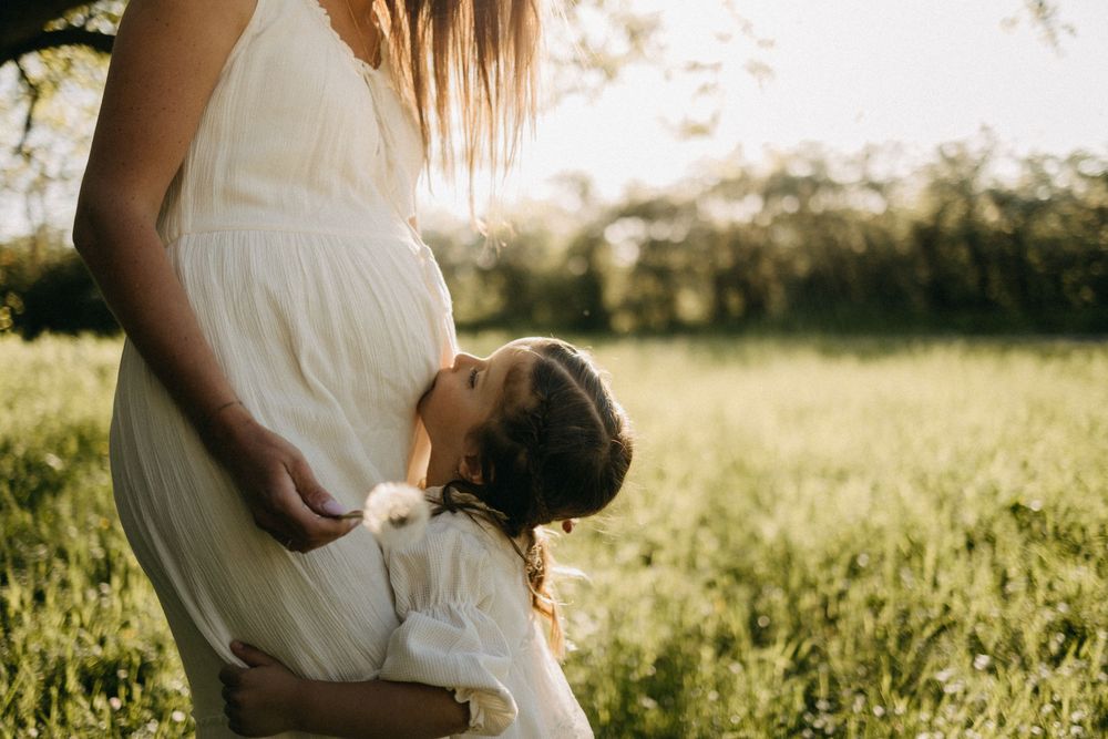 A person in a white dress sits in a sunlit meadow during golden hour.