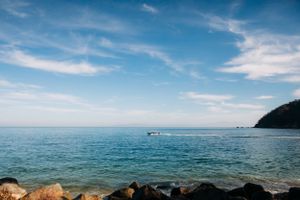 Scenic seascape with turquoise waters, rocky shoreline, and blue skies with wispy clouds over calm Mediterranean waters.