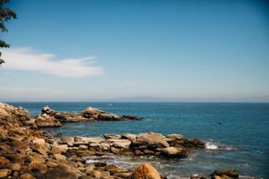 Rocky coastal landscape with large boulders along blue ocean waters under a clear summer sky.