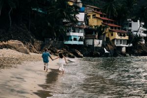 People running together on beach shoreline with colorful hillside homes in Puerto Vallarta, Mexico.