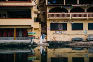 Waterfront building with reflective puddle showing 'BANCO' signage in tropical coastal location during daytime.