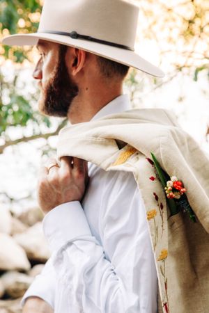 A profile view of someone wearing a white cowboy hat and white button-down shirt with a floral patterned scarf.