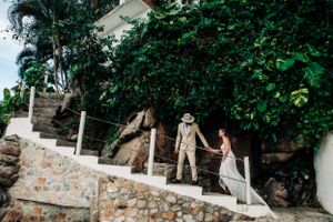 Couple walking down stone stairway surrounded by lush greenery at an outdoor wedding venue in warm natural light.