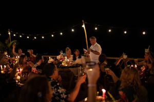 A candlelit celebration at night with party guests dancing under string lights and sparklers.