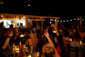 A dark evening reception venue with string lights overhead and guests raising their glasses in celebration.