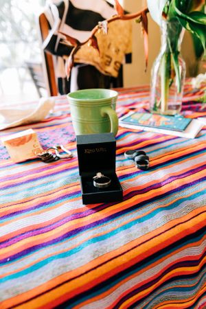 A green coffee mug sits on a colorful striped tablecloth with vibrant orange and blue patterns.