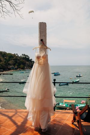 A white wedding dress hangs on display overlooking a picturesque coastal bay with boats in the water.