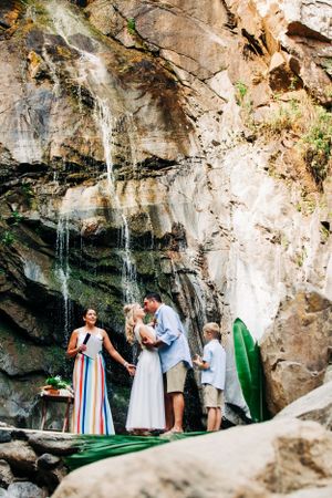 A scenic waterfall cascades down rock cliffs in a natural setting with greenery and people gathered below.