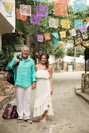 Two people stand on a stone path decorated with colorful papel picado banners hanging overhead in Mexico.