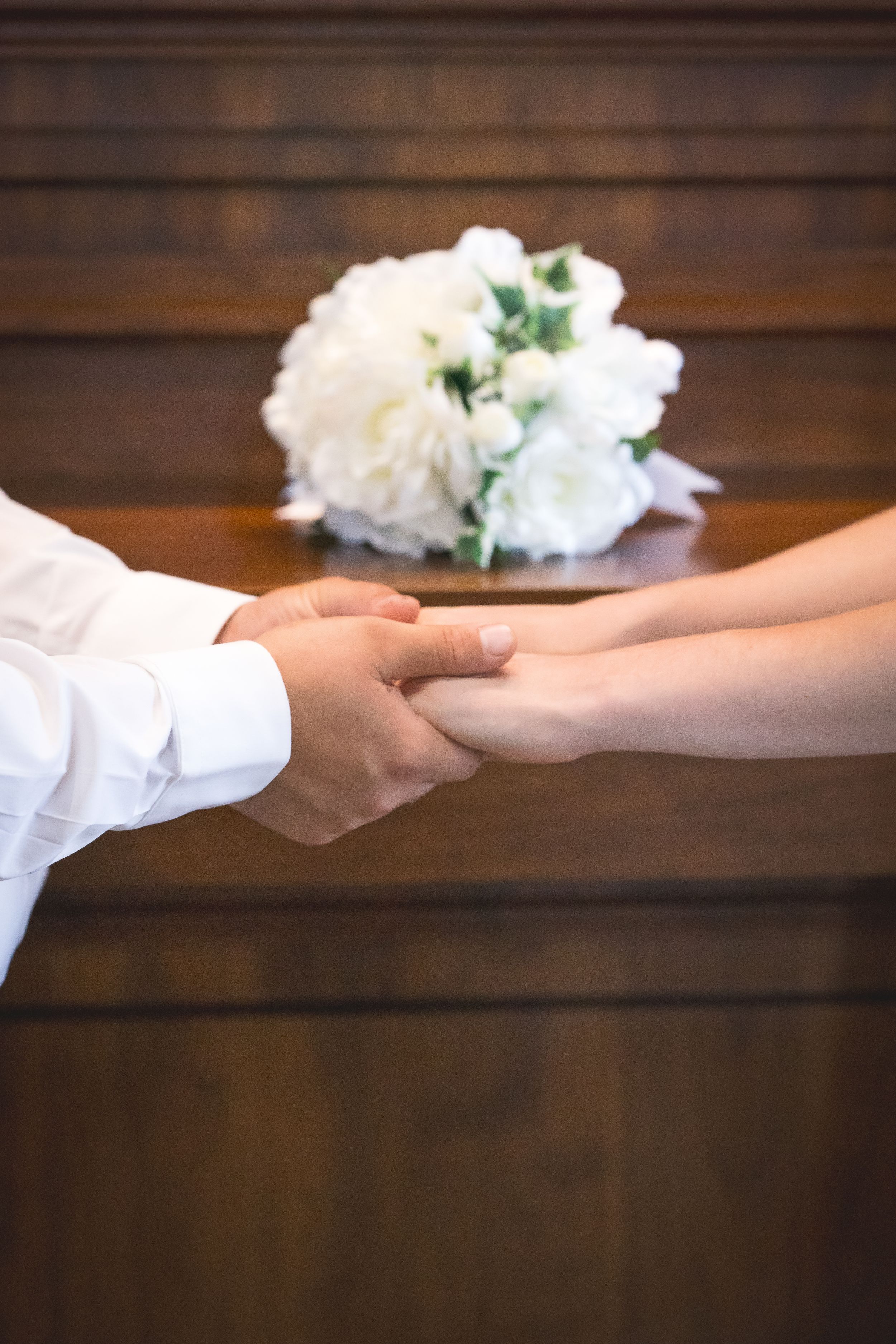 Close-up of hands exchanging rings with white floral arrangement in background.