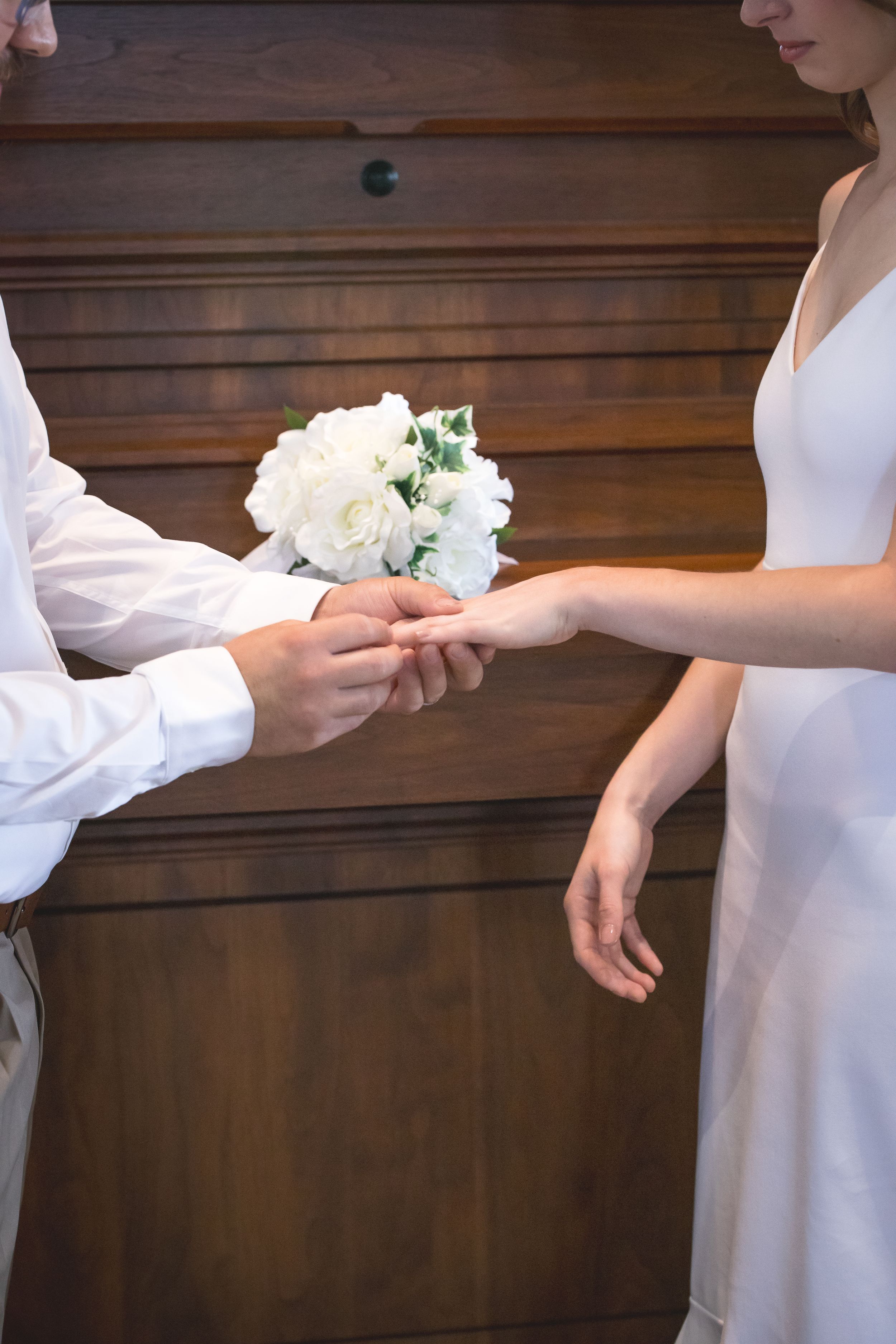 Wedding ceremony sequence showing ring exchange with white floral accents against wooden backdrop.