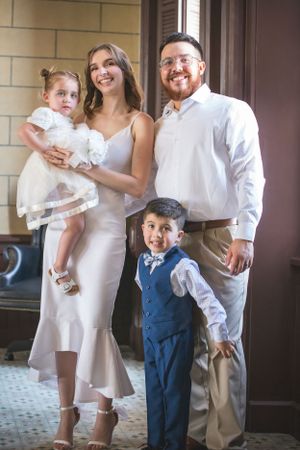 A family of four poses together in formal attire on a porch.