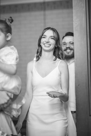 A bride in white dress smiles while holding something during wedding celebration.