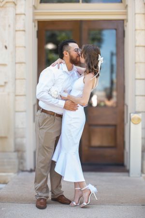 Newlyweds share a romantic kiss outside a historic building entrance.