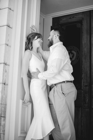 A tender moment between newlyweds against white pillars in black and white photography.